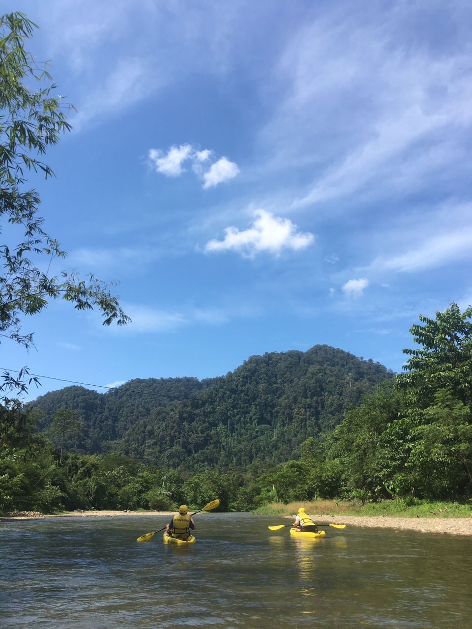 Two kayakers paddling toward the jungle mountains on the Landak River