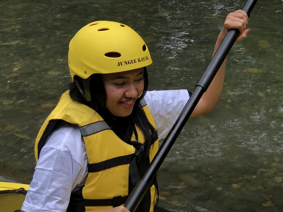 A smiling paddler in a yellow Jungle Kayak helmet and life vest