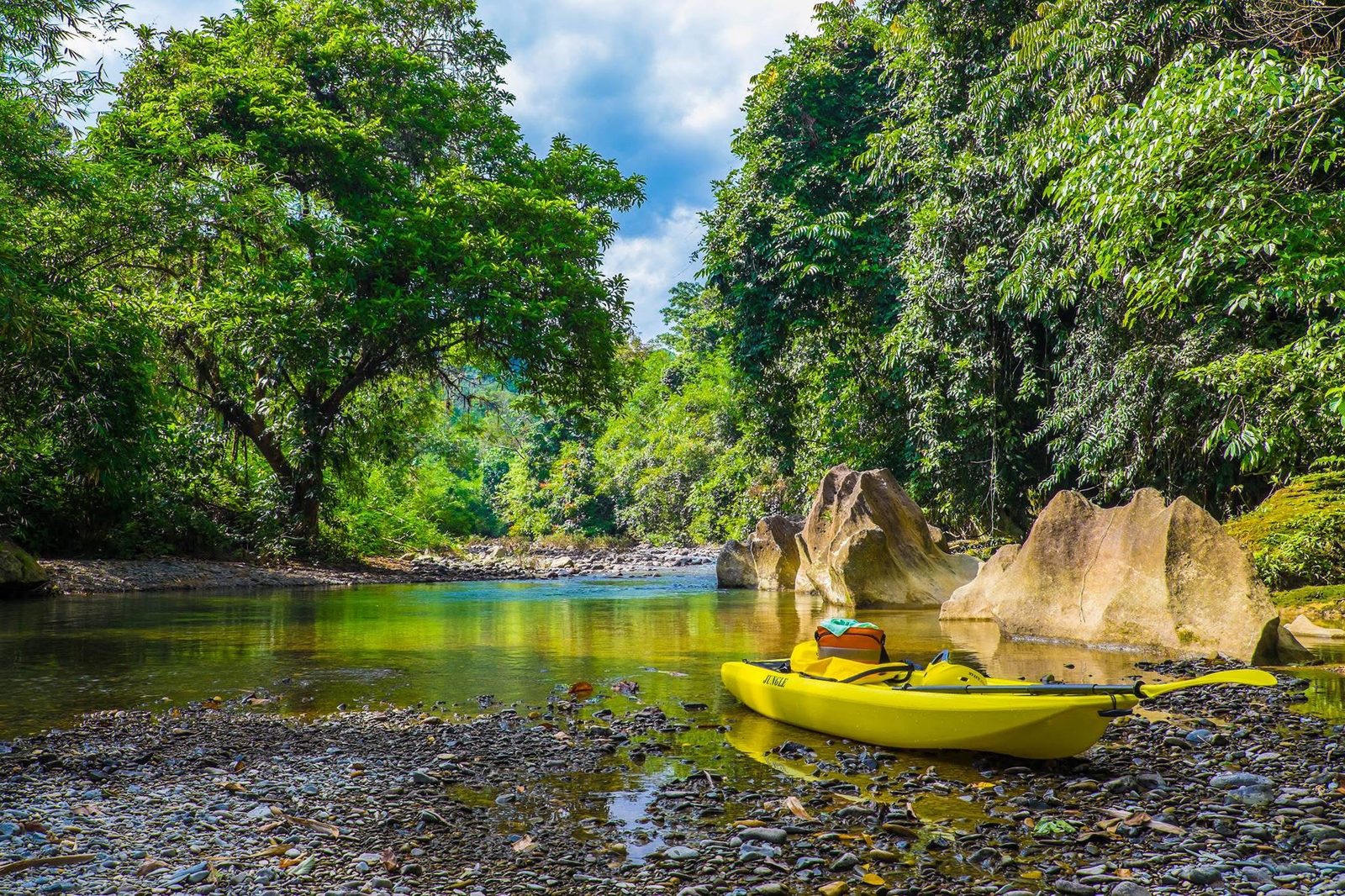 Lone yellow Jungle Kayak boat resting in a quiet bend of the Landak River, surrounded by jungle and giant boulders